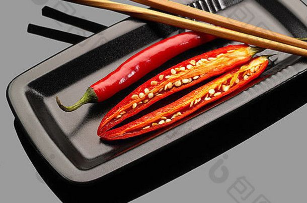 将新鲜的红辣椒放在盘子上，在灰色反光表面上放上筷子