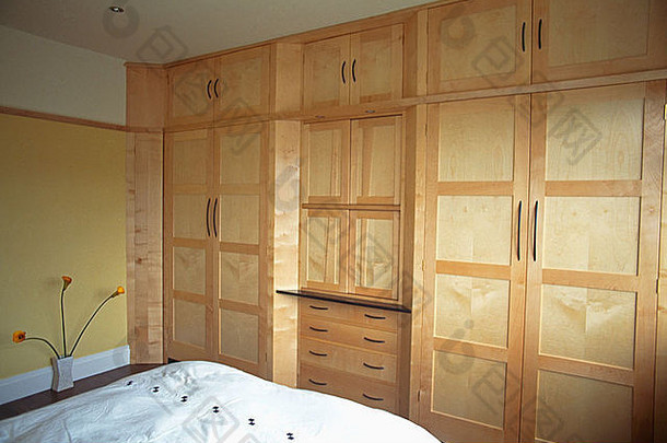 现代卧室中，沿着一面墙的长度，有浅色木制衣柜和储藏室