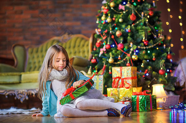 可爱的女孩坐着地板上房间节日圣诞节树持有礼物盒子手圣诞节一年