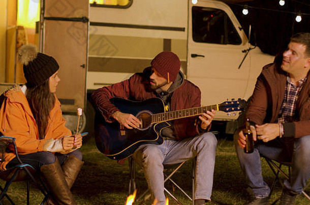 女孩持有棉花糖朋友唱歌吉他营火冷晚上秋天野营山