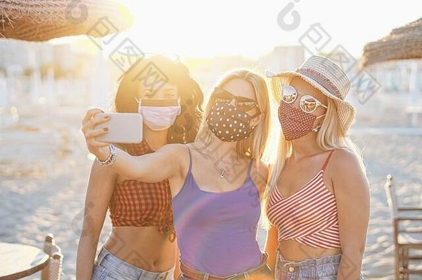 女孩采取自拍脸面具冠状病毒保护青少年假期海滩享受日落多民族的青年甲型肝炎病毒