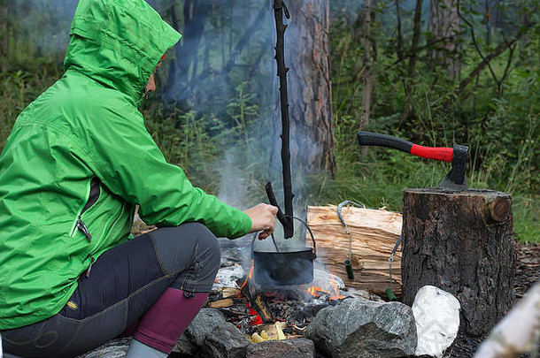 在森林里，一位女旅行者在<strong>烧水壶</strong>做饭。