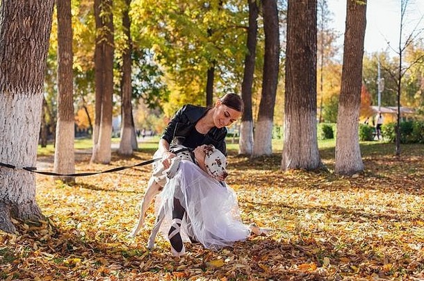 芭蕾舞女演员达尔马提亚狗公园女人芭蕾舞女演员白色芭蕾舞裙子黑色的皮革夹克尖端鞋子秋天公园拥抱