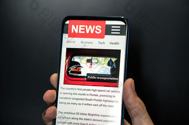 一名男子手持智能手机，屏幕上显示新闻。浏览器中的报纸在线门户。