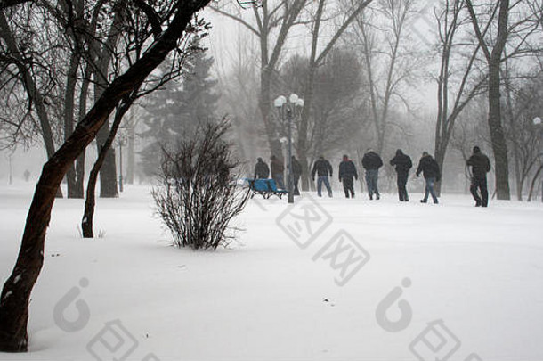 下雪期间，一群人在雪地公园的人行道上行走