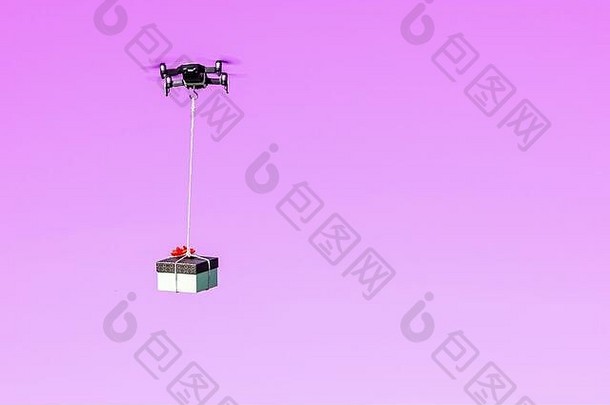多翼无人机带着一个粉红色背景上隔离的礼品盒飞行，这是一种使用无人机的现代快速交付方法的概念
