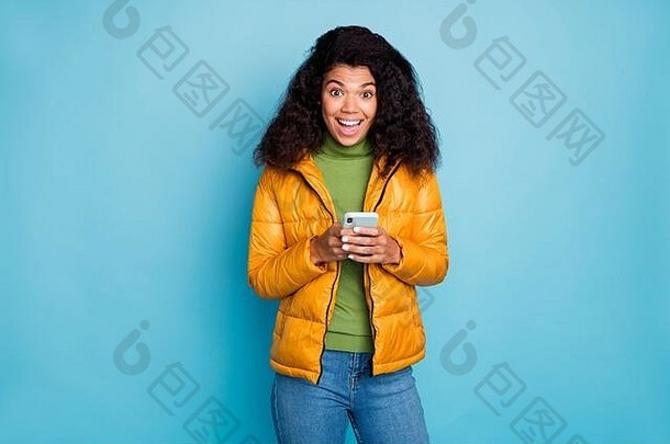照片有趣的黑暗皮肤夫人开放口持有电话手享受博客追随者穿黄色的春天大衣牛仔裤毛衣孤立的蓝色的