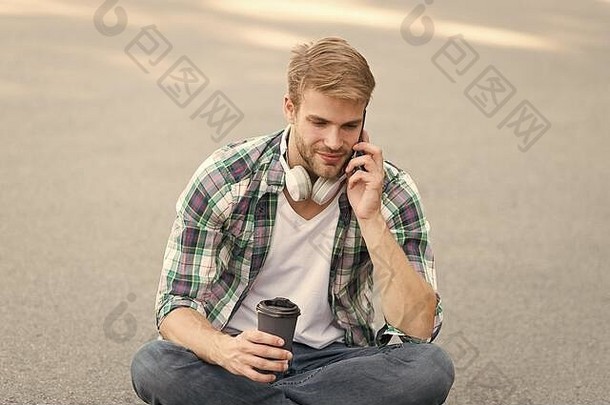 早....共鸣男人。坐地面无忧无虑的学生耳机在线教育听音乐男人。网纹衬衫说话电话学生放松充电咖啡的家伙喝咖啡