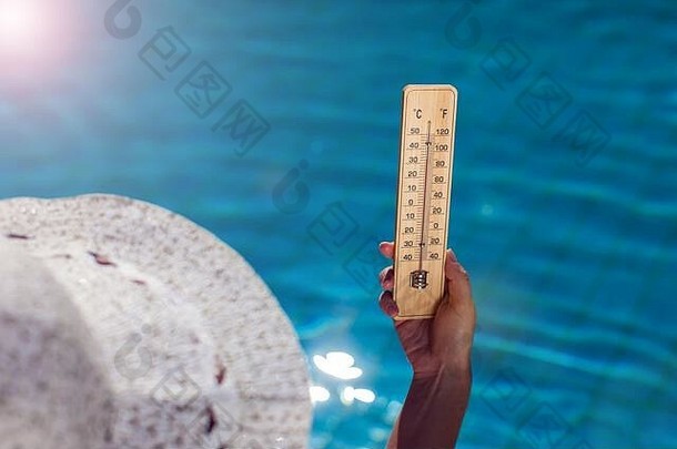 在蓝色泳池背景上拿着温度计的女人。炎热天气与夏季概念