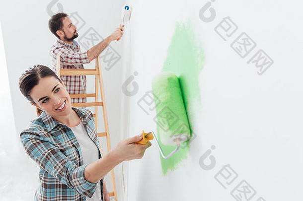 快乐夫妇绘画墙房子男人。站梯女人油漆辊应用明亮的<strong>绿色</strong>油漆