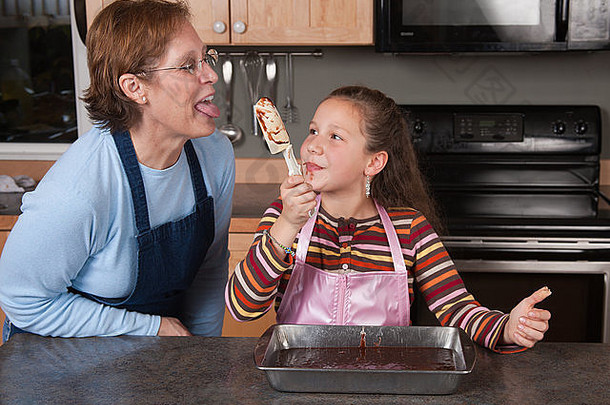 11一年女孩提供勺子巧克力蛋糕混合祖母舔