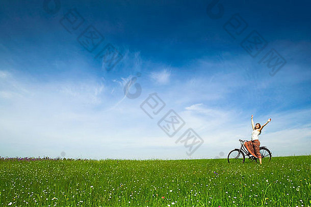 在绿色草地上骑着老式自行车的快乐年轻女子