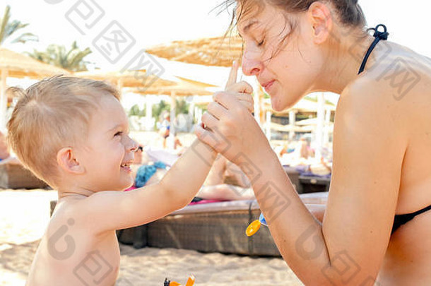 幸福家庭可爱的3岁学步小男孩在海滩上放松，在去皮前涂上紫外线防晒乳液的特写照片