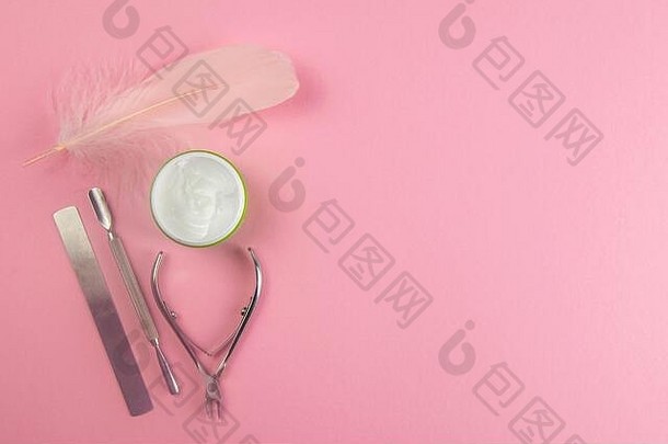 指甲剪、角质层袋、指甲油和护手霜以及一支粉红色的钢笔放在粉红色的桌子上。