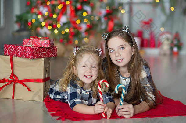 可爱的太棒了女孩姐妹庆祝一年圣诞节关闭圣诞节树完整的玩具时尚的礼服糖果
