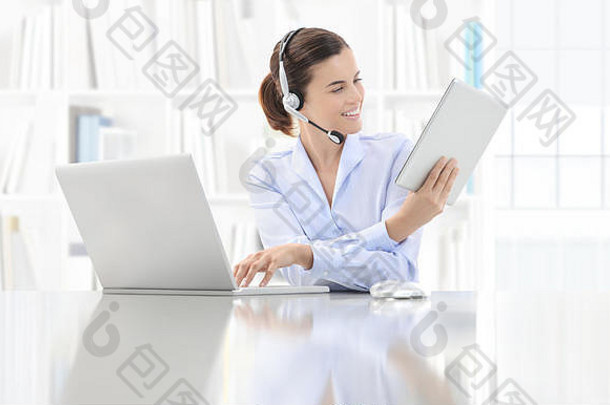 业务微笑女人职员工作办公室桌子上电脑耳机数字平板电脑联系支持概念