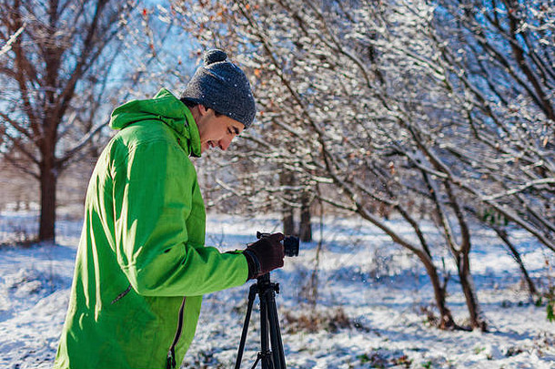 年轻的摄影师用相机和三脚架拍摄冬季森林。喜欢户外活动的年轻人