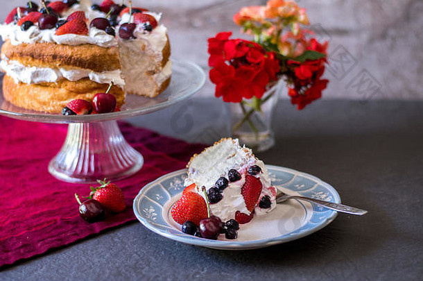 一块美丽的天使食品蛋糕，上面覆盖着鲜奶油和新鲜多彩的浆果，还有鲜花和<strong>水果</strong>