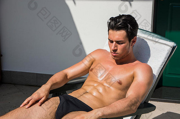 赤膊上阵年轻的男人。干燥热太阳肌肉发达的男人。穿洗澡西装日光浴海滩休息室椅子