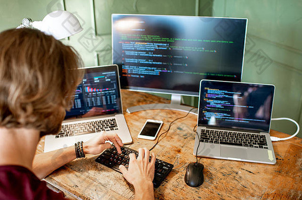 年轻的程序员坐在工作场所编写程序代码，办公室里有三台显示器