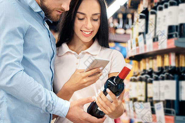 日常购物。夫妇俩一起在超市的酒精部拥抱挑选葡萄酒的女人在智能手机上扫描二维码快乐特写镜头
