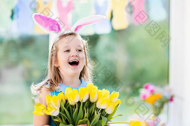 戴着兔子耳朵、手持郁金香花束的快乐小女孩。孩子们庆祝复活节。孩子们正在寻找复活节彩蛋。