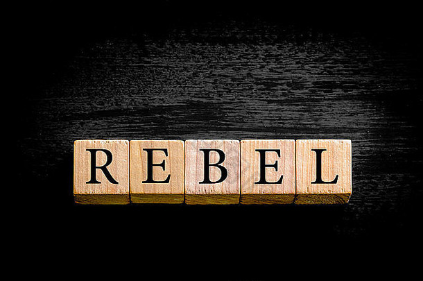 叛逆这个词。木制小立方体，黑色背景上有字母隔离，并留有复印空间。概念形象。