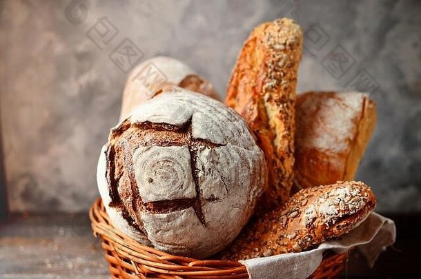 放在柳条篮中的烘焙产品。圆面包、带种子的长面包、不含酵母的纯素面包。木质背景