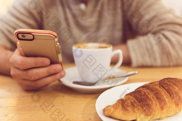 总是保持联系。无法辨认的男子在餐厅吃早餐时喝咖啡和手持智能手机的详细图像。