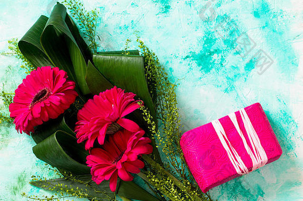 母亲节背景或贺卡。一束红色非洲菊花和一份礼物放在绿松石桌上。平放，俯视背景。