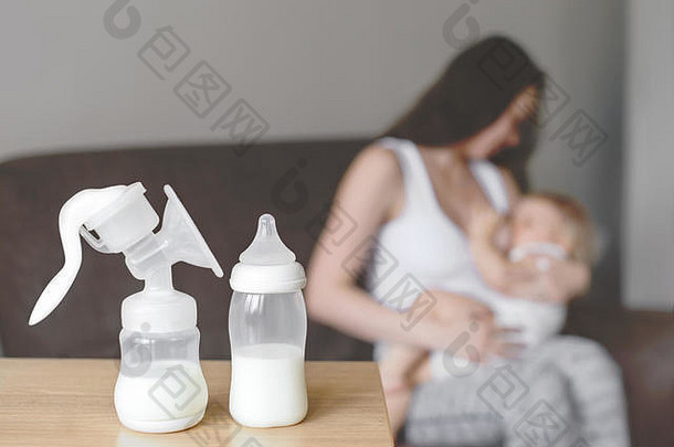 奶瓶和吸奶器以母乳为背景，母亲用手抱着并哺乳婴儿。妇幼保健。