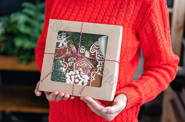 身穿红色毛衣的年轻女子手里拿着圣诞礼物，姜饼。节日包装的饼干。