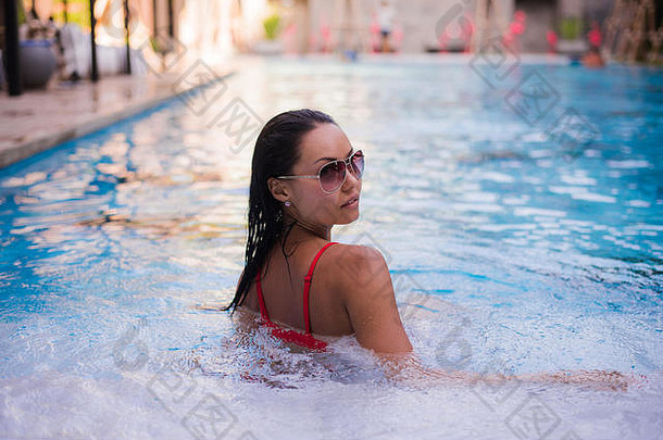 在泳池边度过炎热的夏日。穿着红色比基尼的美丽年轻女子在泳池边放松。