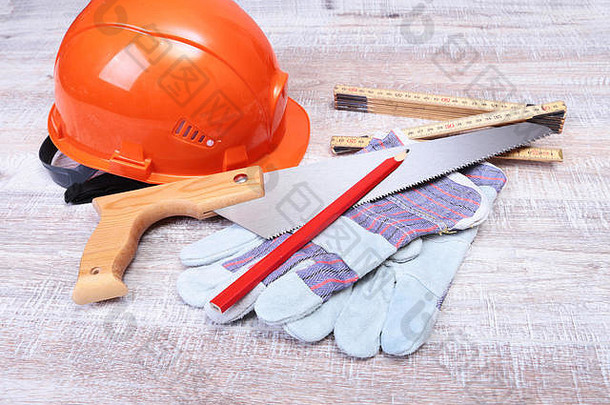 橙色安全帽、降低噪音的耳塞、安全眼镜、手套、钢笔和木制背景上的卷尺。