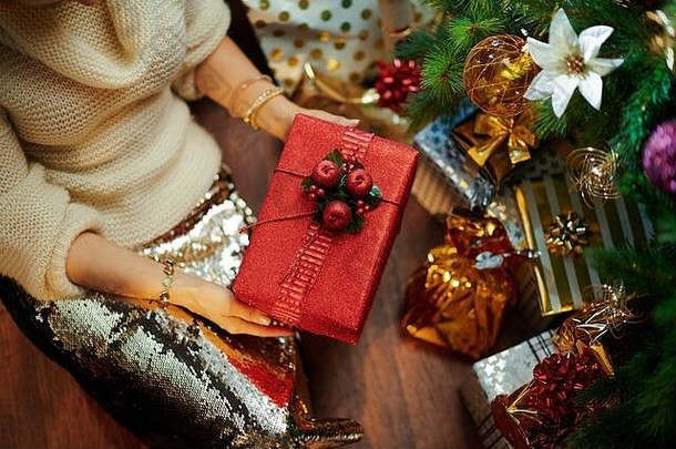 在装饰过的圣诞树下，一位40岁优雅的家庭主妇穿着金色亮片裙子和白色毛衣，在装有圣诞公关的礼品盒附近，拍摄特写