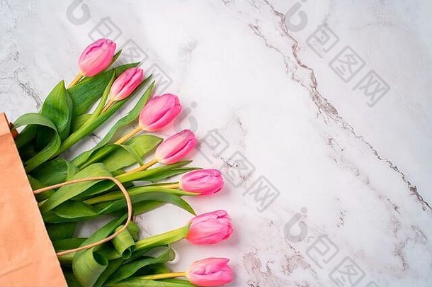 美丽的粉红色郁金香在大理石白色背景上的工艺纸袋中特写，带有空间，俯视图。春、夏、花、色的概念