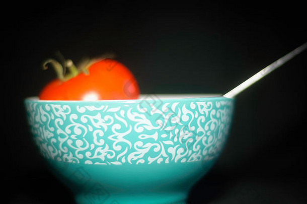 在一个带有绿松石图案和勺子的圆形陶碗中烹饪西红柿的静物画。