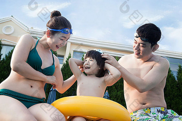 微笑的幸福家庭在泳池边帮儿子戴上护目镜
