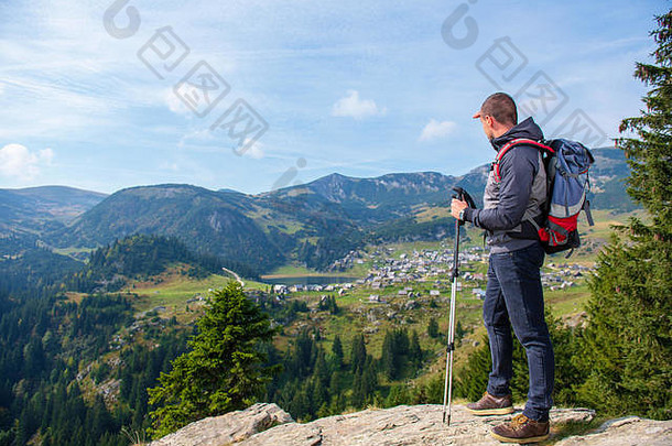徒步旅行者——背着背包和登山杖的年轻人站在悬崖边，看着湖面，后视图