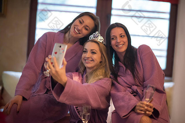 三个年轻美丽快乐的女孩在豪华温泉浴场的单身派对上用香槟自拍