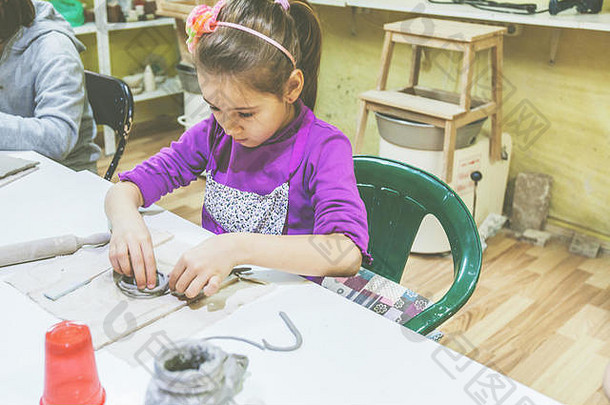 创作小女孩在陶器作坊用粘土工作的肖像。