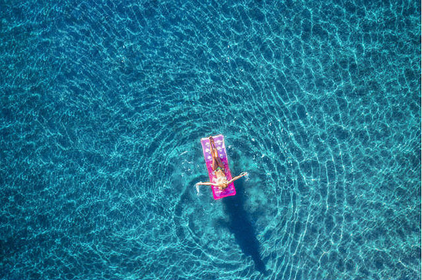 土耳其伊希梅尔透明的绿松石海中，一名年轻女子在粉红色充气床垫上<strong>游泳</strong>的鸟瞰图。<strong>夏日</strong>海景与女孩，亚利桑那州