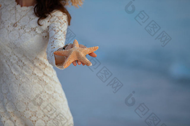 日落时分，一名身着白色连衣裙的女子在海边拍摄海星的特写镜头。