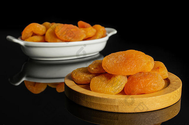在圆形的竹制杯垫上放上大量的干橘杏，放在黑色玻璃上隔离的白色椭圆形陶瓷碗中
