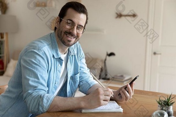 肖像微笑年轻的男人。手机使笔记