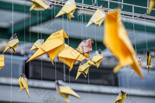 折纸黄橙色纸鹤鸟类悬挂在工业建筑模糊的背景上