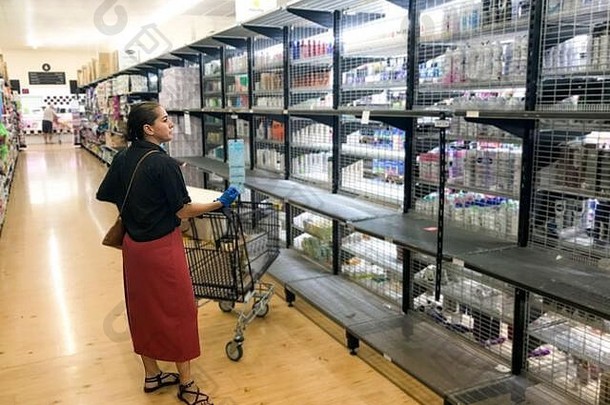 2019冠状病毒疾病爆发。一名妇女站在超市的空货架上，担心冠状病毒大流行。<strong>抢购</strong>使得杂货店空无一人