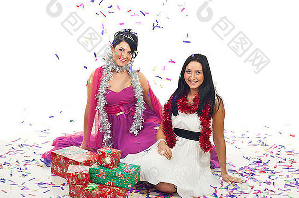 两个穿着优雅连衣裙的漂亮女人坐在地板上，手里拿着圣诞礼物，五彩纸屑掉在上面