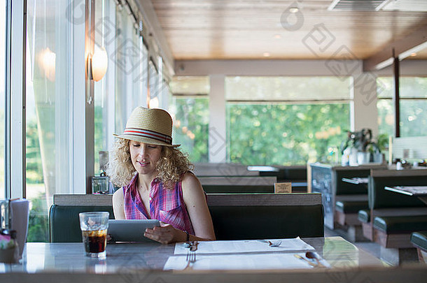 一个戴帽子的女人坐在餐车里，手里拿着一个数字平板电脑，看着屏幕。