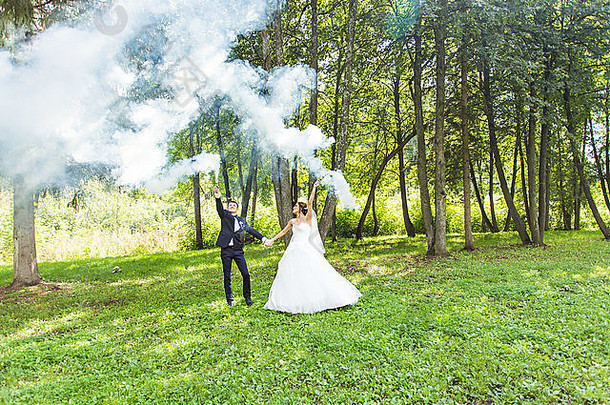 婚礼，爱情，人际关系，婚姻。带着蓝色烟雾微笑的新娘和新郎
